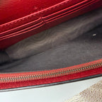 Close-up of a red leather bag with a zipper on a gray surface