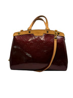 A Louis Vuitton Speedy handbag in glossy burgundy monogram coated canvas with tan leather trim and handles, shown against a neutral light gray background.