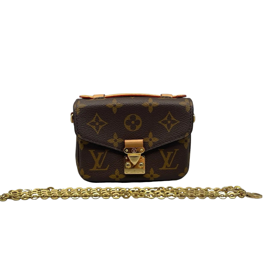 Front view of a miniature Louis Vuitton Micro Metis bag in Monogram canvas, featuring a gold-tone S-lock, Vachetta leather handle, and a removable gold chain strap on a white background.