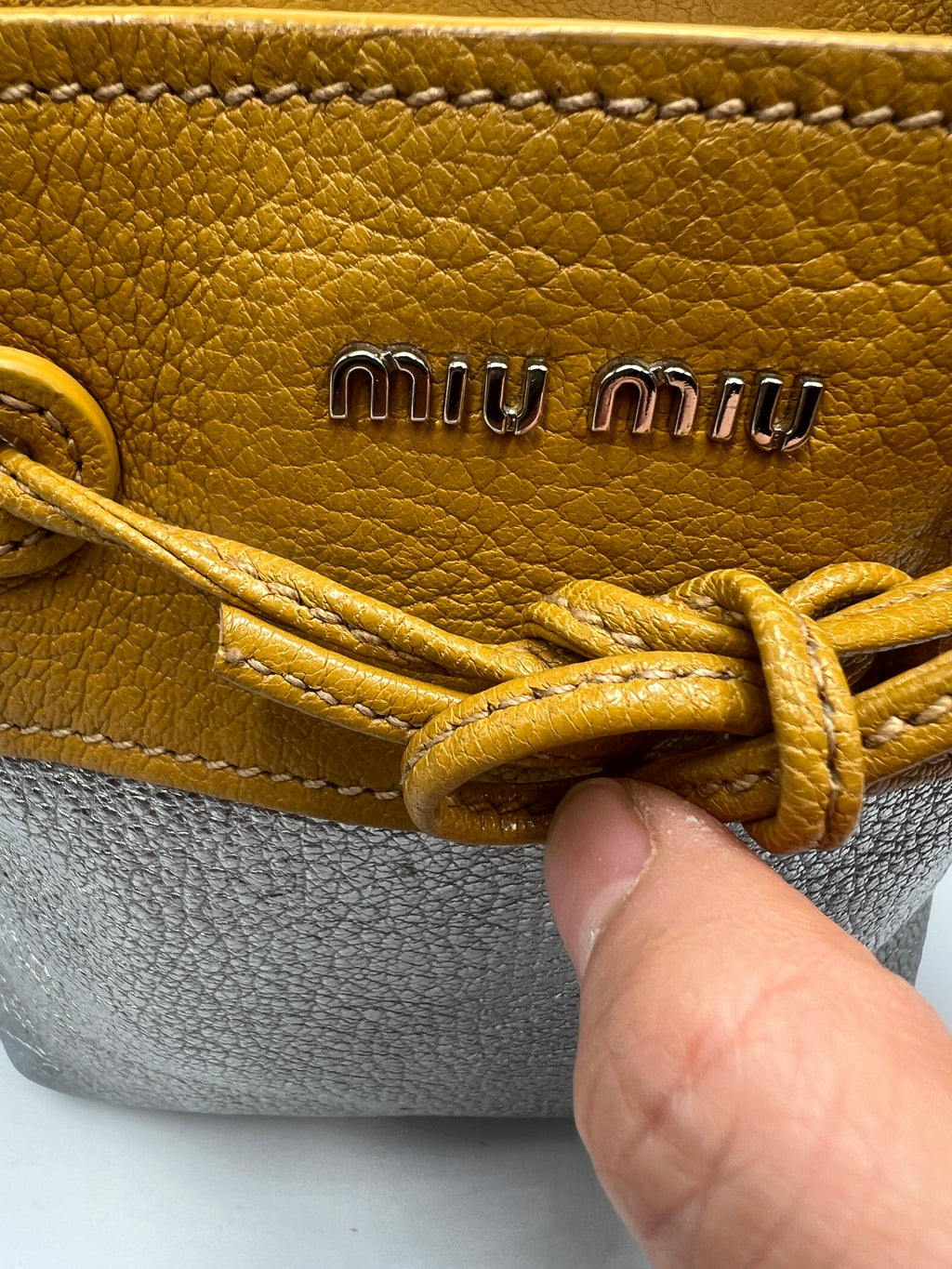 Close-up of a yellow leather shoe with 'Miu Miu' branding, held by a hand.