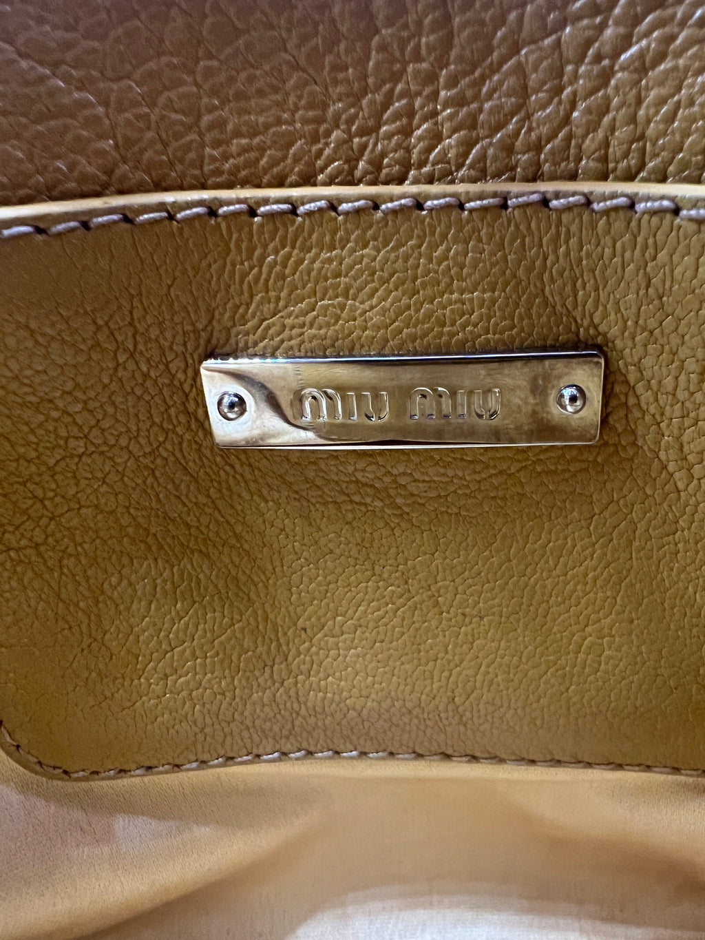 Close-up of a brown leather bag with a visible brand logo. MIUMIU-CROSSBODYBAG