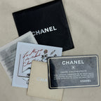 Chanel authenticity documents and packaging laid out on a beige fabric surface, including a black Chanel dust bag, an authenticity card, a receipt, a beige insert card, and a black authenticity card with white text.