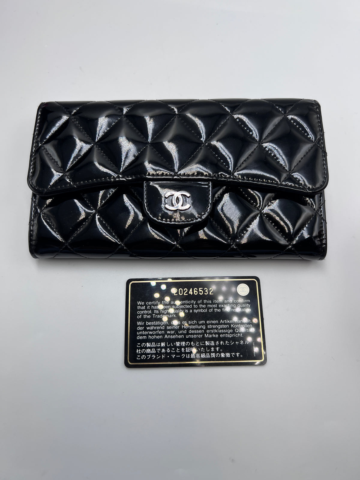 Front view of a Chanel Classic Flap Wallet in black quilted patent leather with silver CC logo emblem and authenticity card.