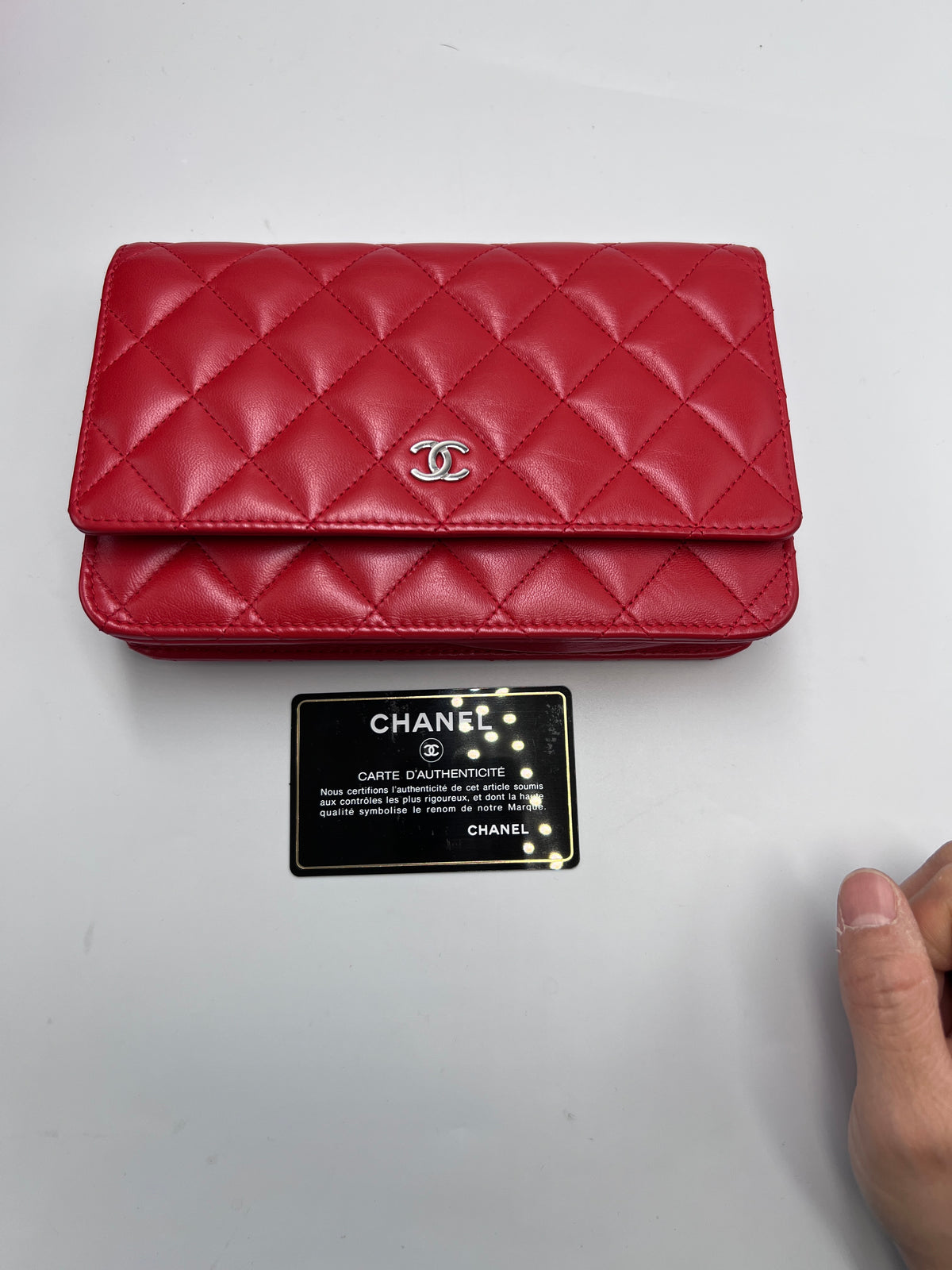 Front view of a Chanel Classic Wallet on Chain in red quilted lambskin leather with silver CC logo and authenticity card.