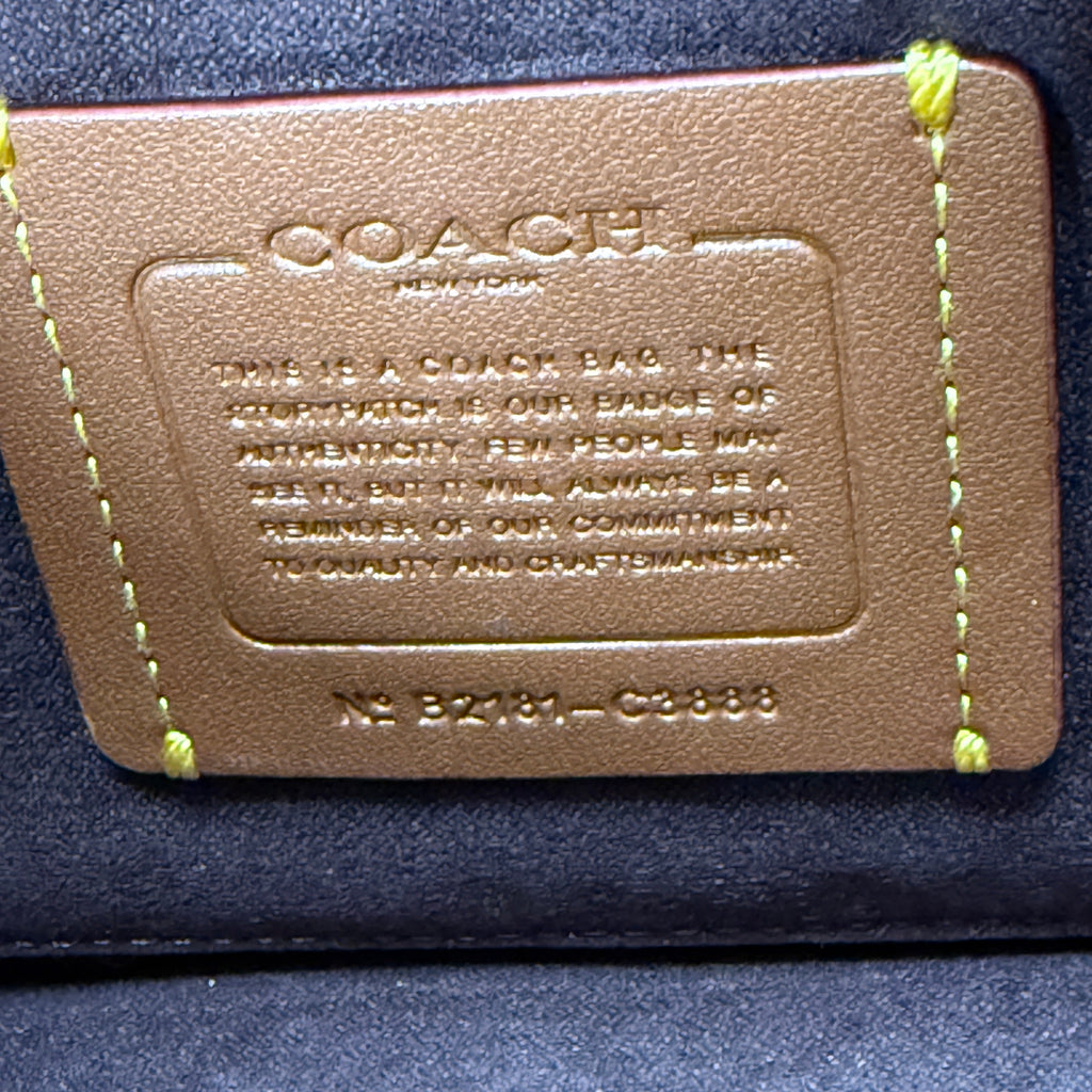 A close-up of a Coach leather card holder or wallet insert with yellow stitching, showing the embossed Coach logo and text on a dark blue fabric background.