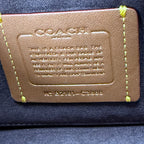 A close-up of a Coach leather card holder or wallet insert with yellow stitching, showing the embossed Coach logo and text on a dark blue fabric background.