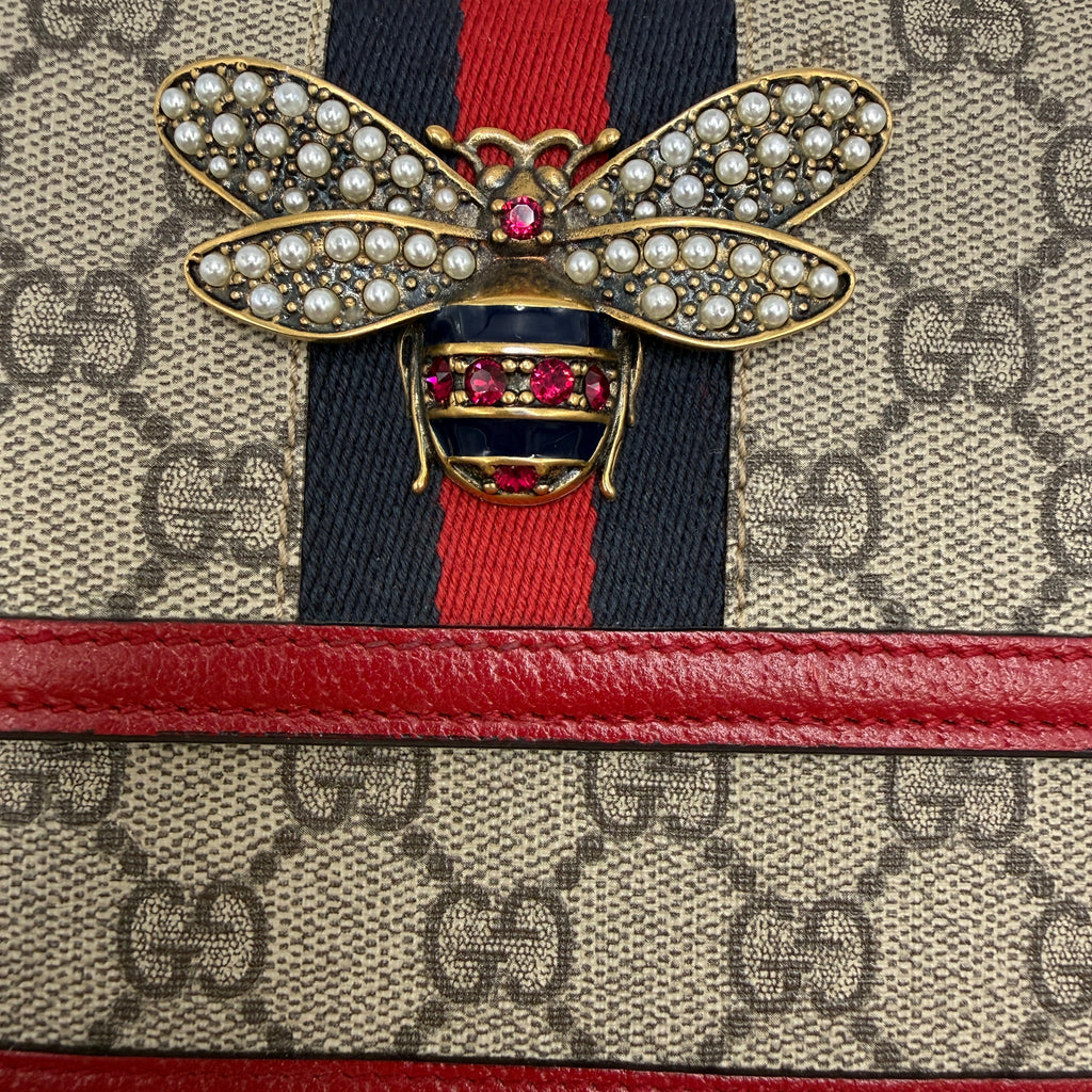 used Designer handbag with a prominent bow brooch featuring red and gold colors.