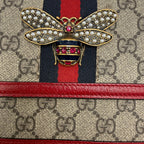 used Designer handbag with a prominent bow brooch featuring red and gold colors.