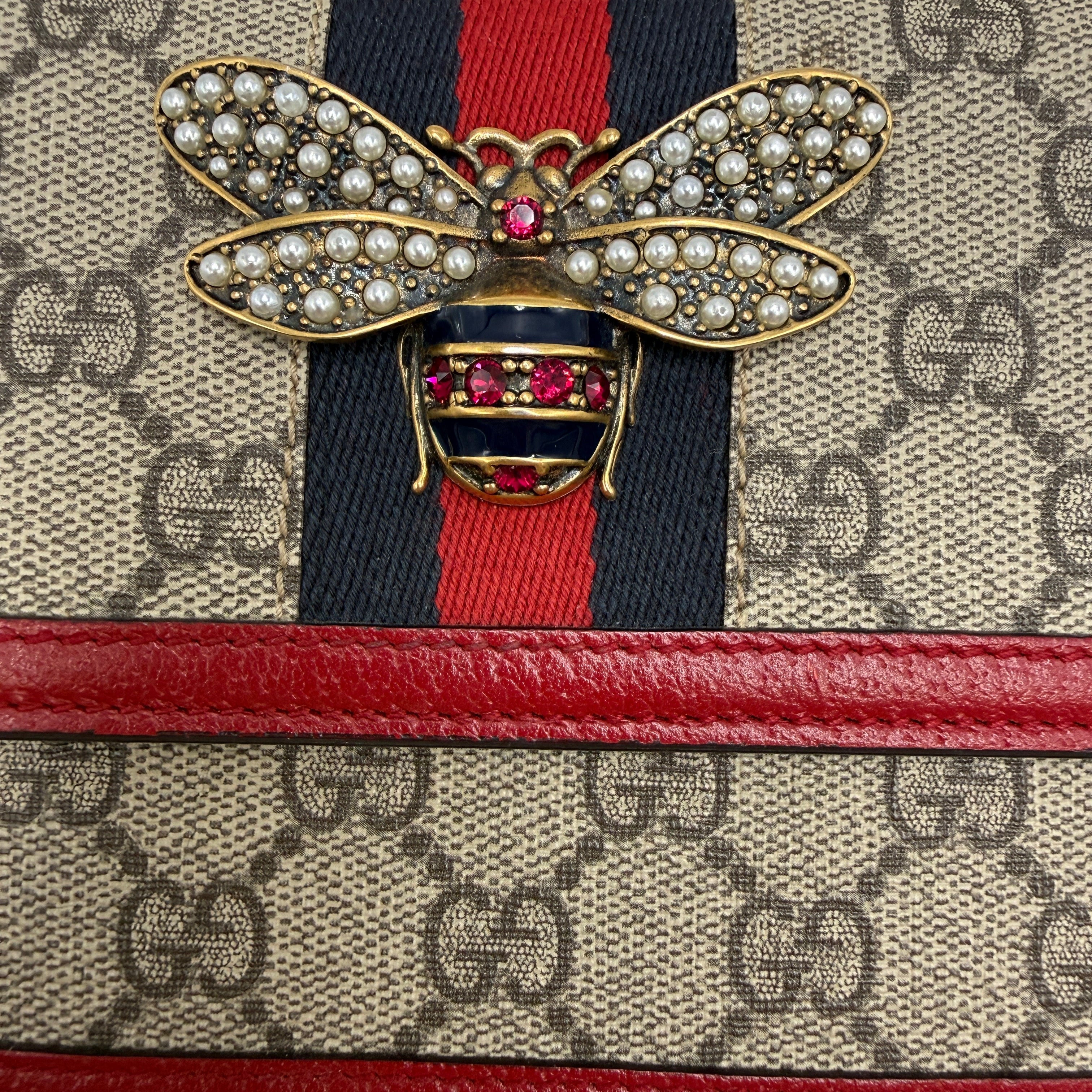 used Designer handbag with a prominent bow brooch featuring red and gold colors.