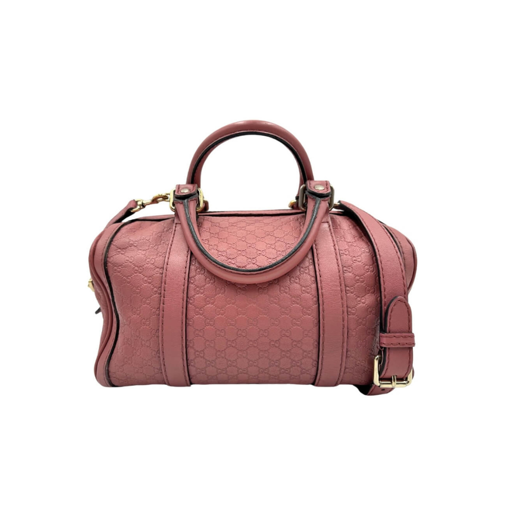 Front view of a structured Gucci Joy Boston bag in pink Micro Guccissima embossed leather with top handles and a crossbody strap.