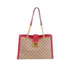 A Gucci GG Supreme tote bag in beige and brown monogram canvas with bright red leather trim and handles, featuring gold-tone hardware and a front lock closure, shown on a plain white background.