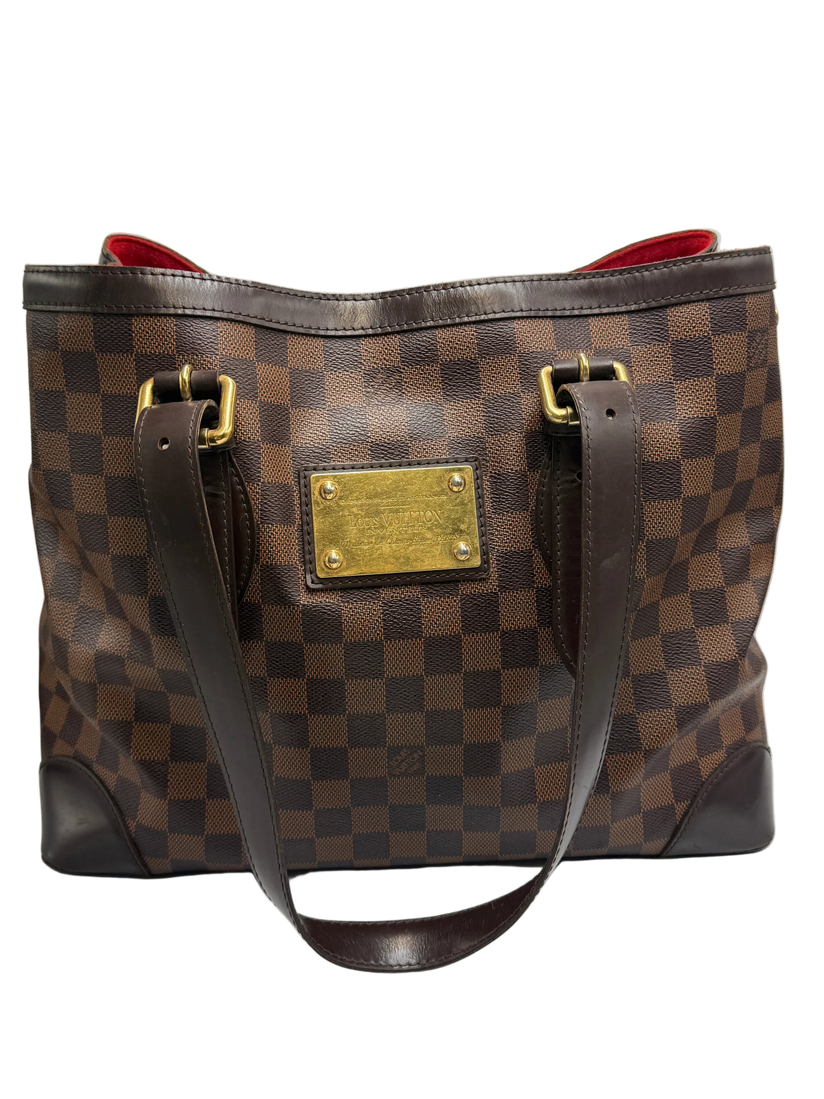 A Louis Vuitton Damier Ebene canvas tote bag with a brown checkerboard pattern, dark brown leather trim, gold-tone hardware, and a red interior lining, shown against a neutral light gray background.