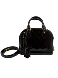 A Louis Vuitton glossy patent leather Alma handbag in black, featuring gold-tone hardware and a matching black monogrammed leather strap coiled beside it on a light gray background.