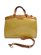 A Louis Vuitton Monogram Tote bag in glossy mustard yellow patent leather with tan leather trim and gold-tone hardware, shown with its detachable shoulder strap on a light gray background.