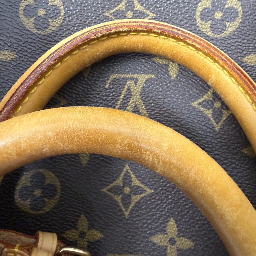 Close-up of a Louis Vuitton monogram canvas bag with a curved tan leather handle, showing the classic dark brown and beige LV pattern.