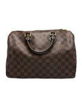 A brown checkered leather handbag with dark brown handles and gold-tone hardware, photographed against a neutral gray background.
