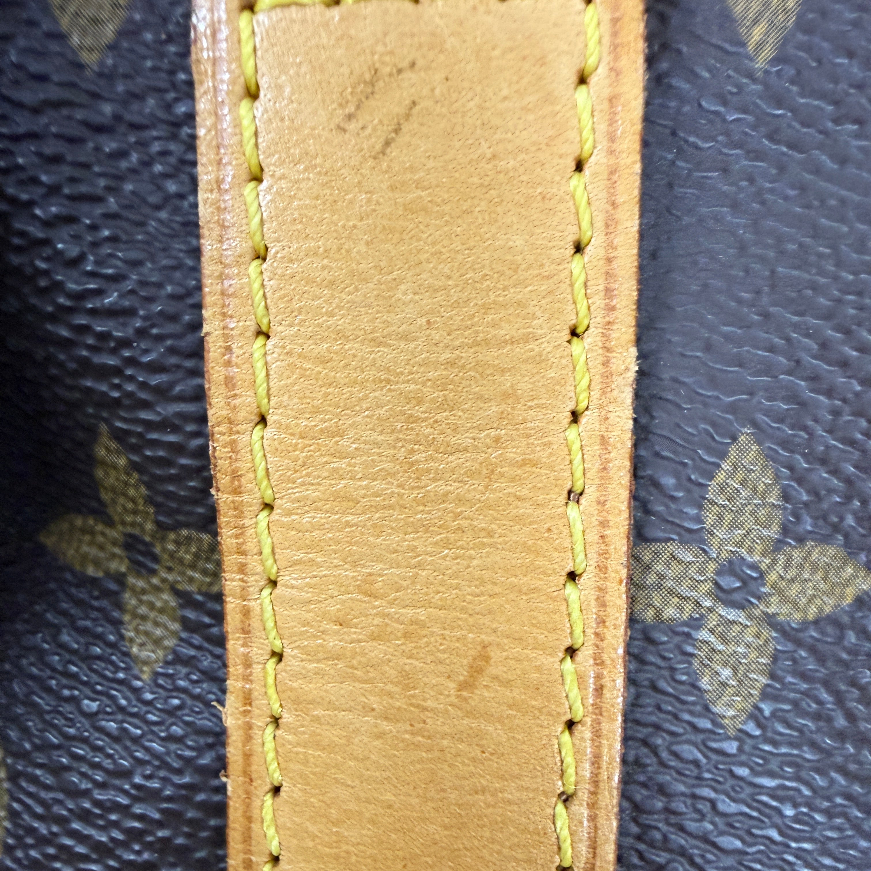 Close-up of a tan leather strap with yellow stitching on a dark brown Louis Vuitton monogram canvas background.
