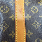 Close-up of a Louis Vuitton monogram canvas bag with a tan leather trim and visible scuffing on the leather strip.