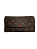 A Louis Vuitton monogram canvas long wallet or card holder with a brown leather texture, tan monogram pattern, and a small red snap button closure, shown on a plain light gray background.