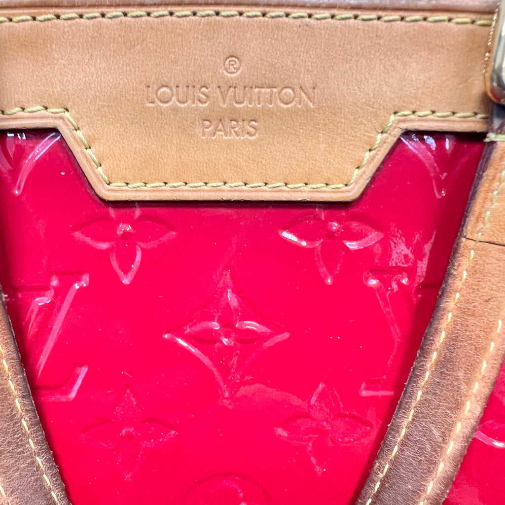 Close-up of a Louis Vuitton handbag showing a bright pink monogram coated canvas body and a tan leather trim with the Louis Vuitton Paris logo embossed on the upper panel.