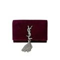A burgundy velvet clutch bag featuring a silver-tone YSL logo embellished with clear crystals and a dangling silver tassel, shown against a plain white background.
